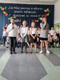Czwórka dzieci stoi na tle grupy, chłopiec z dziewczynką mówią do mikrofonów