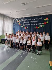 grupa dzieci na tle granatowej ściany z napisem, nad ich głowami białe confetti