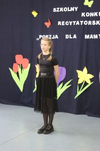 Dziewczynka ubrana na czarno, w tle napis i duże kwiaty