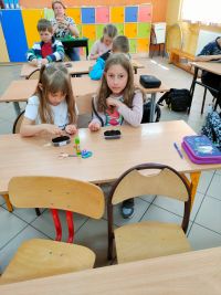 Dzieci siedzą w ławkach i wysiewają nasiona