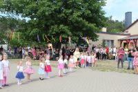 Małe dziewczynki w kolorowych strojach, przy budynku szkoły stoją ludzie