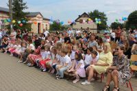 Dzieci i dorośli siedzą na ławkach i oglądają występy