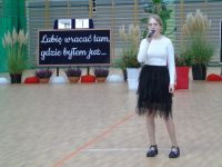 Dziewczynka ubrana na galowo, trzyma mikrofon, śpiewa