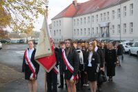 dzieci stoją trójkami w kolumnie, pierwsza róka to poczet sztandarowy szkoły